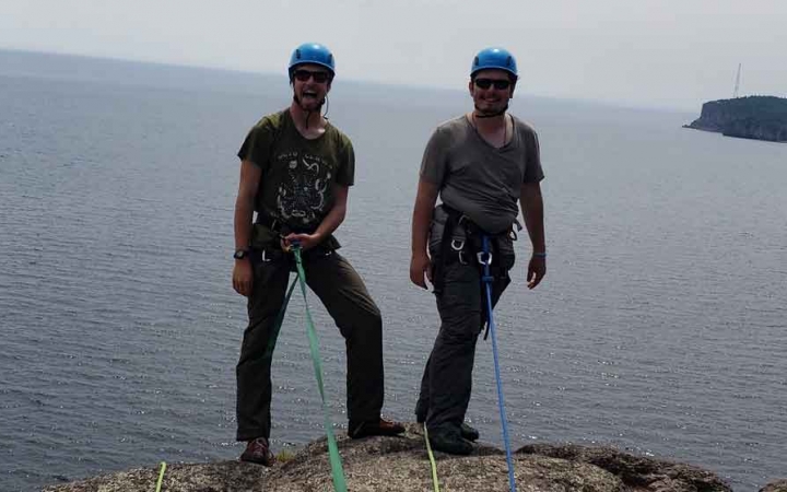 two gap year students preparing to rock climb stand on a cliff above a lake